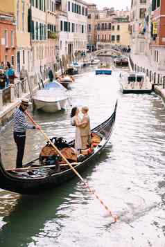 威尼斯意大利10月意大利婚礼威尼斯用凤尾船运送卷新娘新郎经典木贡多拉狭窄的威尼斯运河新婚夫妇站船后视图