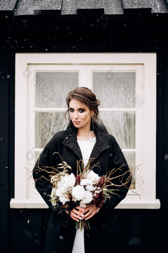 肖像新娘白色丝绸婚礼衣服黑色的外套新娘的花束手黑色的木房子白色窗口下雪目的地冰岛婚礼