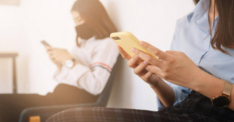 亚洲年轻的女人聊天智能手机穿面具坐着距离保护科维德病毒社会距离感染风险