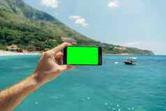 男人的手持有智能手机空白屏幕背景绿色植物蓝色的海