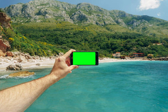 男人的手持有智能手机空白屏幕背景绿色山蓝色的海