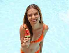 有吸引力的微笑女孩吃冰棒冰流行形式西瓜片游泳池夏天假期概念