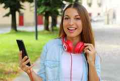 快乐女孩持有聪明的电话选择音乐移动应用程序在户外相机