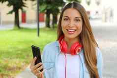 年轻的女人持有聪明的电话选择音乐移动应用程序在户外相机