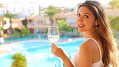 微笑年轻的女人喝白色酒户外度假胜地阳台快乐美丽的女人白色衣服夏天旅行假期相机