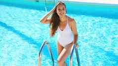 微笑女孩白色泳衣未来游泳池水美丽的健康的年轻的女人泳装摆姿势在游泳池边夏天假期