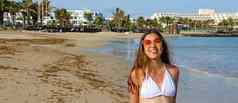 漂亮的年轻的晒黑女人白色比基尼太阳镜摆姿势户外夏天海滩全景横幅视图