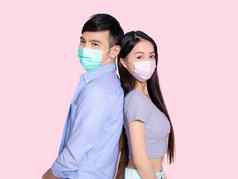 年轻的夫妇站穿医疗面具孤立的粉红色的背景
