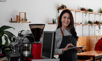 快乐的年轻的亚洲女人老板持有数字平板电脑站咖啡馆年轻的企业家概念上的