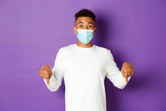 概念冠状病毒检疫生活方式惊讶非裔美国人男人。医疗面具指出手指相机显示复制空间站紫色的背景