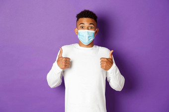 概念科维德流感大流行社会距离惊讶非裔美国人的家伙医疗面具显示竖起大拇指批准站紫色的背景