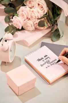 女人手持有笔准备好了写粉红色的玫瑰笔礼物粉红色的心白色表格爱概念圣情人节一天概念母亲的一天概念