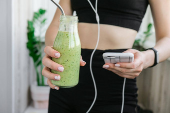 年轻的millenial女人检查智能手机喝素食主义者奶昔喝<strong>排毒</strong>女人瑜伽练习首页在线学费清洁吃重量损失健康的节食食物概念保持健康的