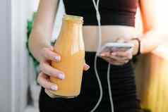 年轻的millenial女人检查智能手机喝素食主义者奶昔喝排毒女人瑜伽练习首页在线学费清洁吃重量损失健康的节食食物概念保持健康的