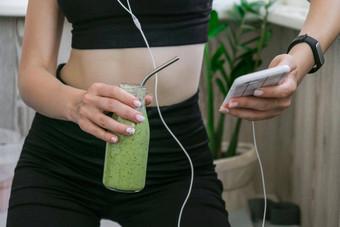 年轻的millenial女人检查智能手机喝素食主义者奶昔喝排毒女人瑜伽练习<strong>首页</strong>在线学费清洁吃重量损失健康的节食食物概念保持健康的