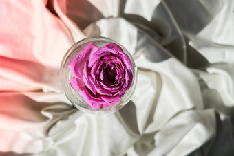 酒玻璃填满粉红色的花petalson白色丝绸织物最小的现代生活假期概念情人节女士一天背景设计
