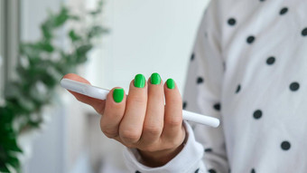 修剪整齐的女手时尚的绿色指甲持有移动电话智能手机技术时尚的现代设计修指甲过来这里指甲皮肤护理美治疗指甲护理时尚的颜色