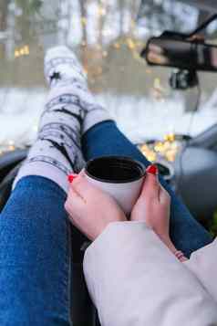 女人腿袜子手持有热水瓶杯咖啡茶冬天车圣诞节袜子加兰散焦灯