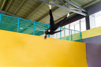 年轻的女人业余杂技运动员跳锻炼蹦床在室内现代爱好健身概念