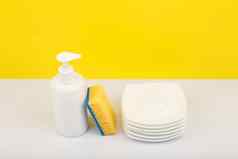 洗碗洗涤剂白色瓶桩碟子清洁海绵黄色的背景