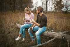 夫妇游客喝热喝自然微笑高加索人男人。女人休息在户外持有金属野营杯子热咖啡茶热水瓶坐着树森林草坪上