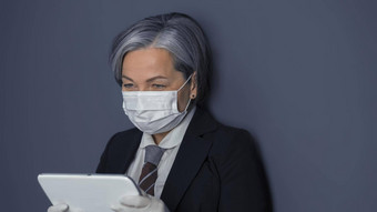 成熟的女商人保护<strong>面具</strong>数字平板电脑灰色的头发的女人阅读新闻工作平板电脑电脑站灰色的墙背景健美的图像