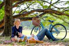 美丽的女孩坐的男朋友斜倚自行车回来大树花园