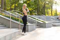 体育运动健身年轻的高加索人女人穿着运动服装喝水塑料瓶站户外夏天公园阳光背景