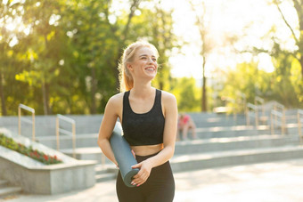 运动苗条的女人运动型衣服黑色的紧身裤前站混凝土楼梯持有瑜伽席休息练习体育运动健身概念