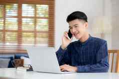 年轻的亚洲男人。会说话的电话工作首页移动PC电脑自由笔记本互联网在线说话智能手机国内生活业务沟通概念