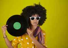 女人太阳镜非洲式发型发型持有乙烯基磁盘黄色的背景