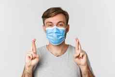 概念流感大流行科维德社会距离充满希望的担心的家伙医疗面具交叉手指好运气使站白色背景