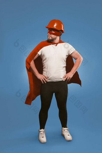 超级英雄工程师男人。穿红色的头盔面具角站手臀部孤立的褪了色的牛仔布蓝色的背景