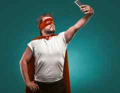超级英雄男人。需要自拍移动手机男人。超级英雄服装红色的面具斗篷孤立的比斯开湾绿色背景