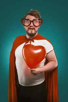 超人爱持有大红色的心积极的男人。超级英雄服装心形的眼镜提出了比斯开湾绿色背景情人节一天概念