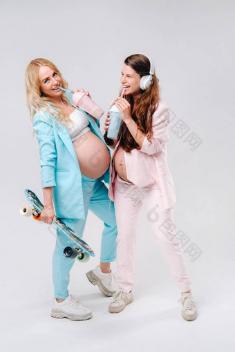 怀孕了女孩绿松石粉红色的西装眼镜汁滑冰耳机站灰色的背景