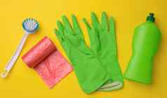 橡胶绿色手套清洁红色的垃圾塑料袋卷塑料瓶洗涤剂黄色的背景