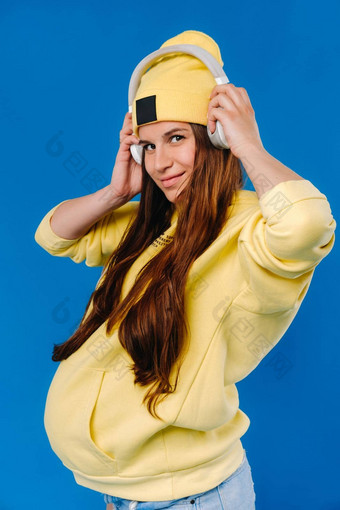 怀孕了女孩黄色的夹克耳机站蓝色的背景