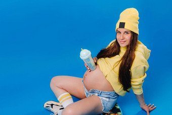 怀孕了女孩黄色的衣服玻璃汁坐在滑板蓝色的背景