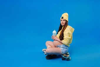 怀孕了女孩黄色的衣服玻璃汁坐在滑板蓝色的背景