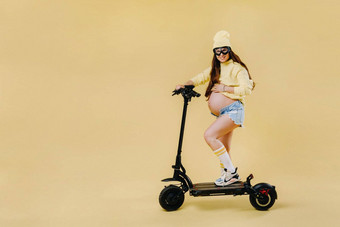 怀孕了女孩黄色的衣服电<strong>踏板车</strong>孤立的黄色的背景