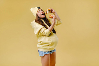 怀孕了女孩黄色的衣服汉堡包手黄色的背景