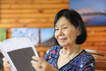 上了年纪的亚洲女人微笑阅读杂志