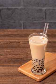 受欢迎的台湾喝泡沫牛奶茶木薯珍珠球喝玻璃稻草木表格灰色的砖背景关闭复制空间