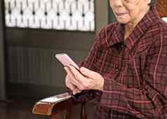 亚洲上了年纪的女人坐着现代智能手机使连接首页生活技术关闭