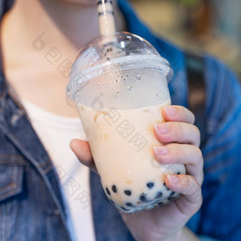 年轻的女孩牛仔布夹克喝棕色（的）糖味木薯珍珠泡沫牛奶茶玻璃稻草晚上市场台湾关闭散景
