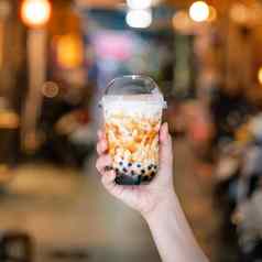 年轻的女人持有喝棕色（的）糖味木薯珍珠泡沫牛奶茶玻璃稻草晚上市场台湾关闭散景