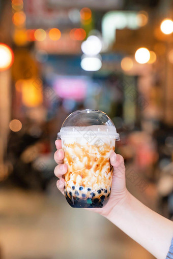 年轻的女人持有喝棕色（的）糖味木薯珍珠泡沫牛奶茶玻璃稻草晚上市场台湾关闭散景