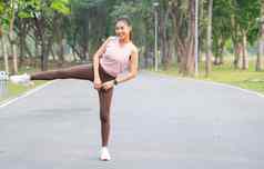 亚洲体育运动女人站行动拉伸腿一边相机微笑路公园花园早....光