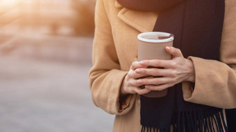 关闭女人的手持有杯咖啡穿米色外套街女时尚肖像时尚的年轻的女人穿秋天外套红色的贝雷帽在户外秋天配件